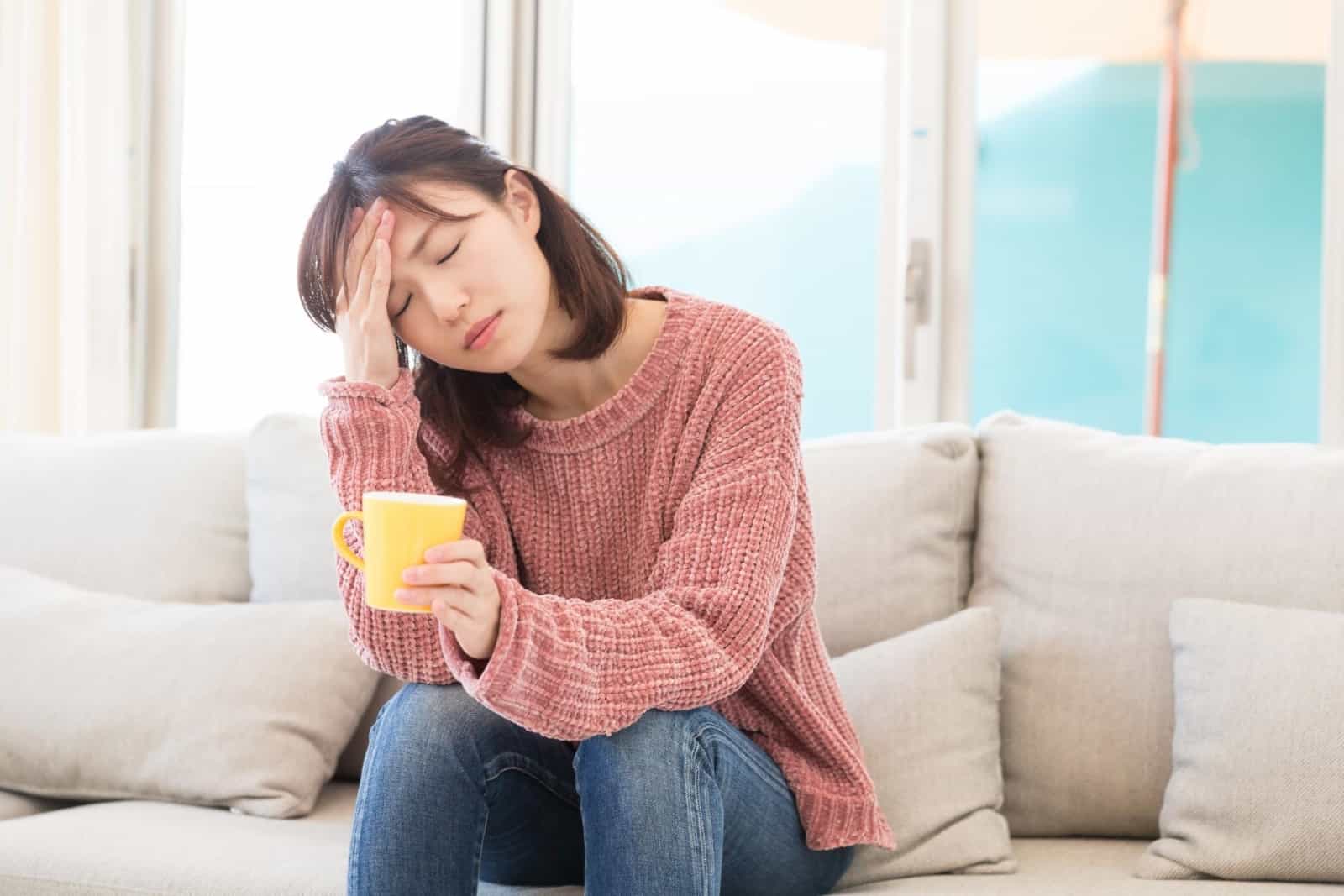 SIBO fatigue: Woman with a headache sitting on a couch and holding a mug