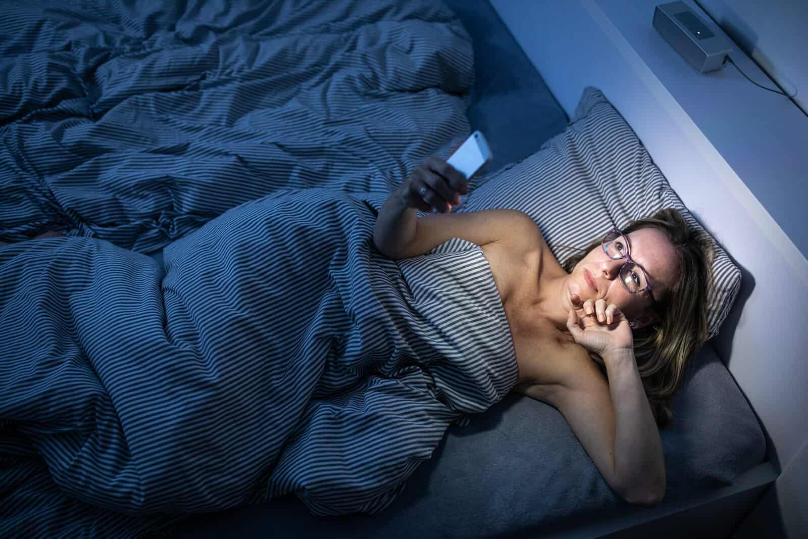 How long does melatonin last: woman using her phone while in bed